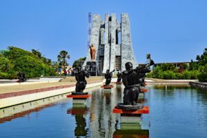 Group of statues depicting people, positioned in front of a flowing water fountain in a public space.